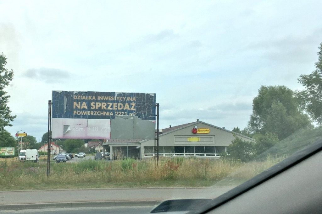Połamany płot i obskurny baner witają przyjezdnych