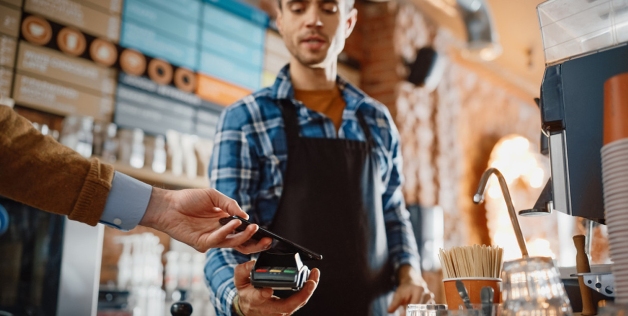 fot. Trzymający terminal barman przyjmuje od klienta płatność telefonem
